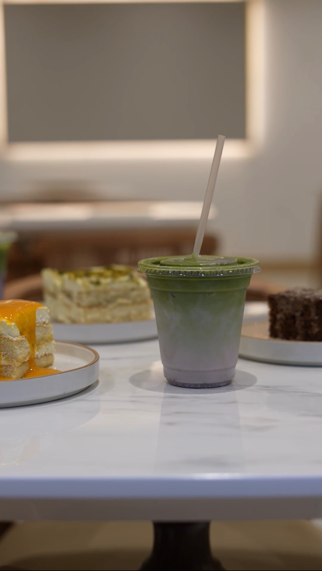 Layered ombré matcha latte beside slices of homemade cake